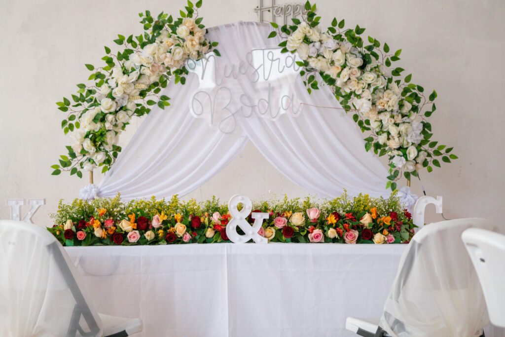 Beautifully decorated wedding table adorned with roses, greenery, and draped white fabric.