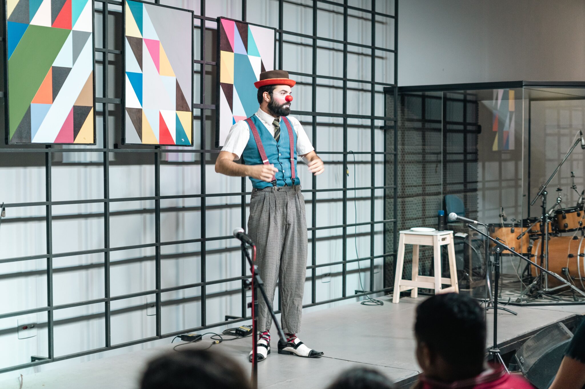 Entertaining clown in costume with a red nose and green vest performing on a stage indoors.