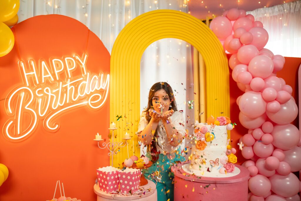 Joyful birthday party featuring colorful balloons, cake, and a young woman celebrating with confetti.