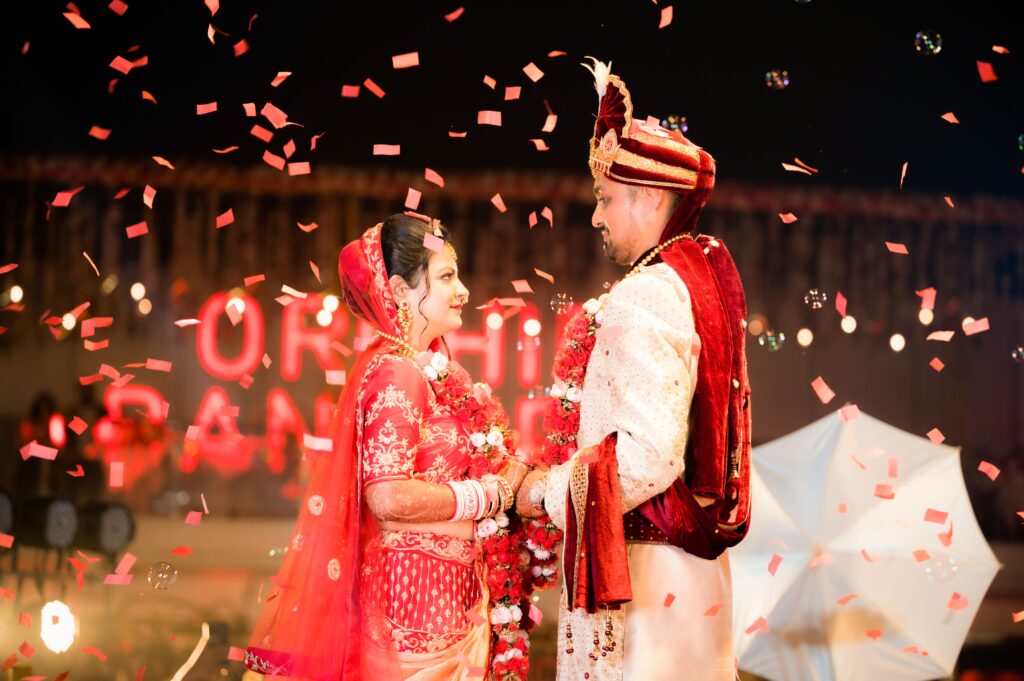 A joyful Indian couple in traditional attire during a vibrant nighttime wedding celebration.