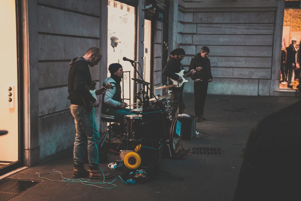 A group of street musicians performing with instruments on a city sidewalk during the evening.