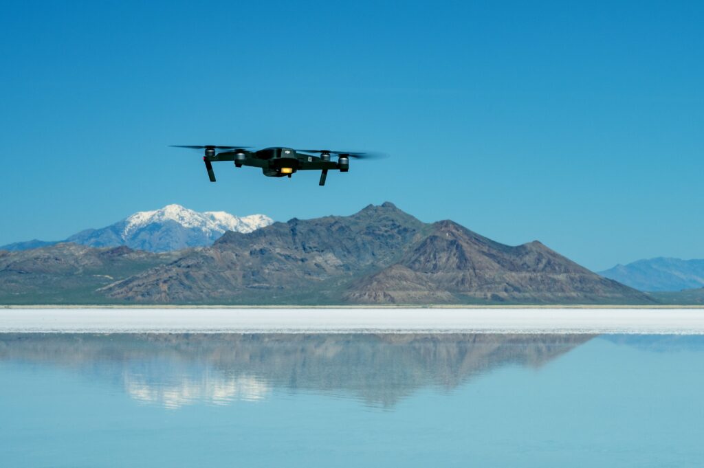 A drone hovering above a reflective lake with majestic mountains in the background.