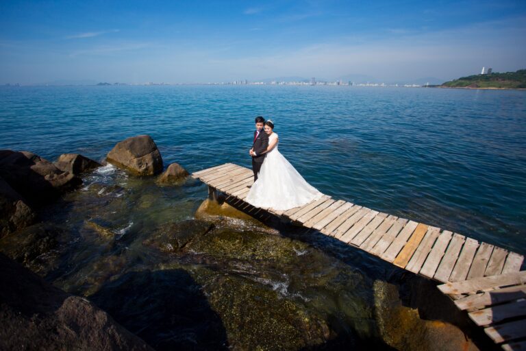 Bride and groom pose on a rustic pier by the sea in Hội An, Vietnam.