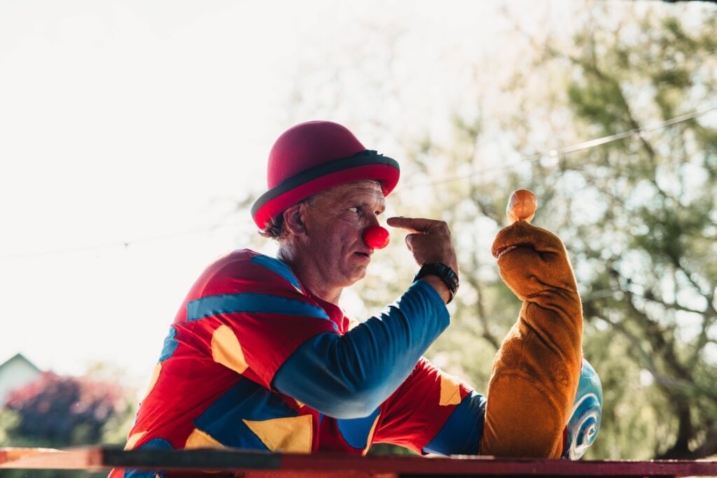 A cheerful clown with a puppet entertaining outdoors, emphasizing fun and creativity.