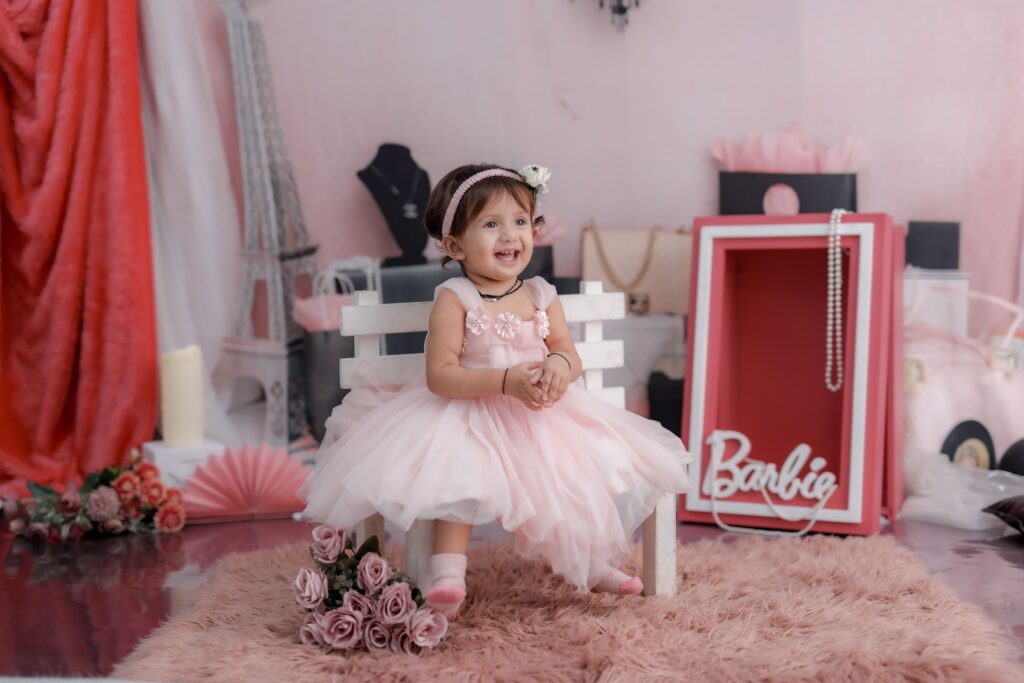 Delightful toddler girl in a pink dress smiling in a charming indoor setup.