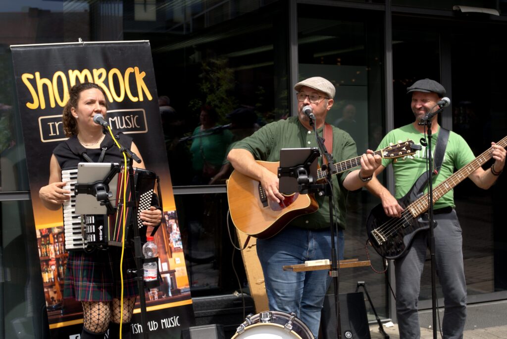 A vibrant outdoor performance by an Irish band featuring accordion, guitar, and bass.