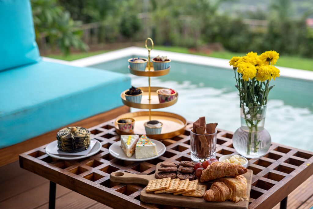 Outdoor brunch setup with delicious pastries, snacks, and flowers by the pool.