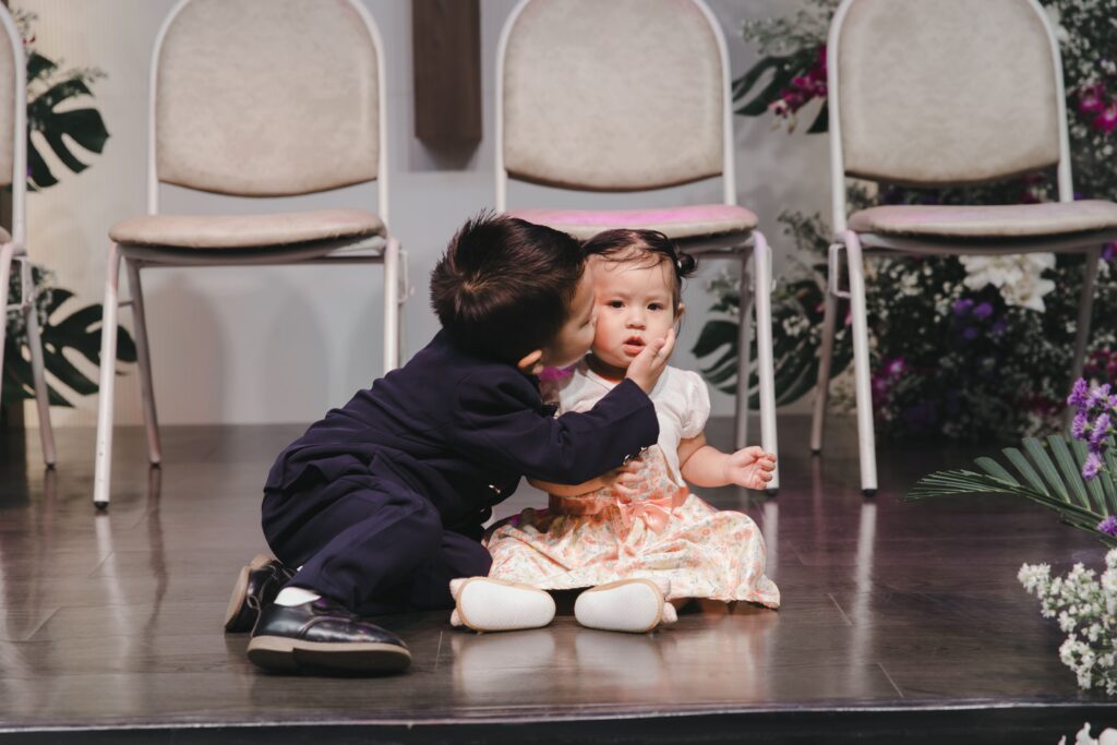 A young sibling pair shares a tender moment at a decorated indoor venue in Thailand.