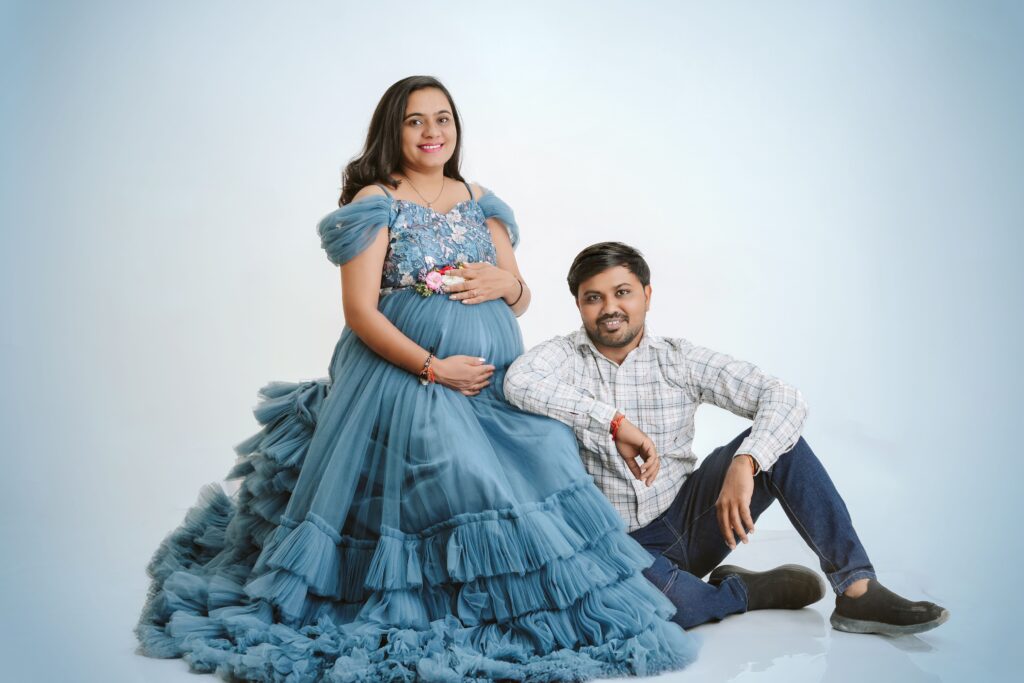 Charming maternity portrait featuring a couple in elegant blue attire with a serene backdrop.