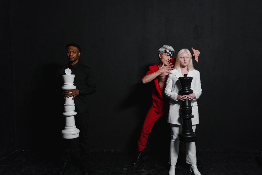 Three people posed indoors with giant chess pieces representing a strategic game concept.
