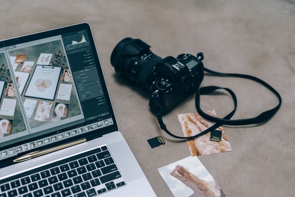 Laptop with editing software alongside DSLR camera and memory cards on a desk.