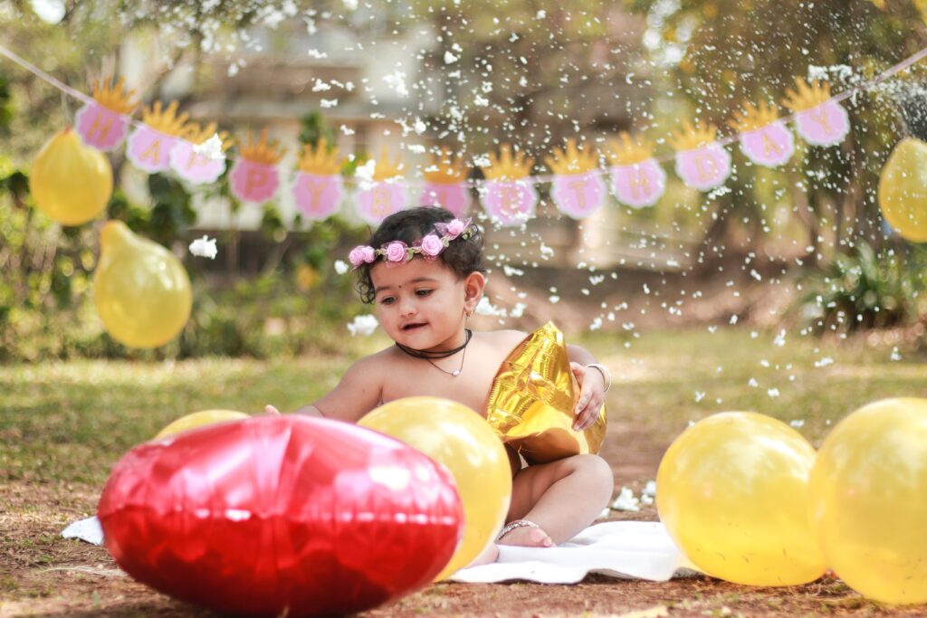 Adorable baby enjoying a fun outdoor birthday celebration with balloons and decorations.